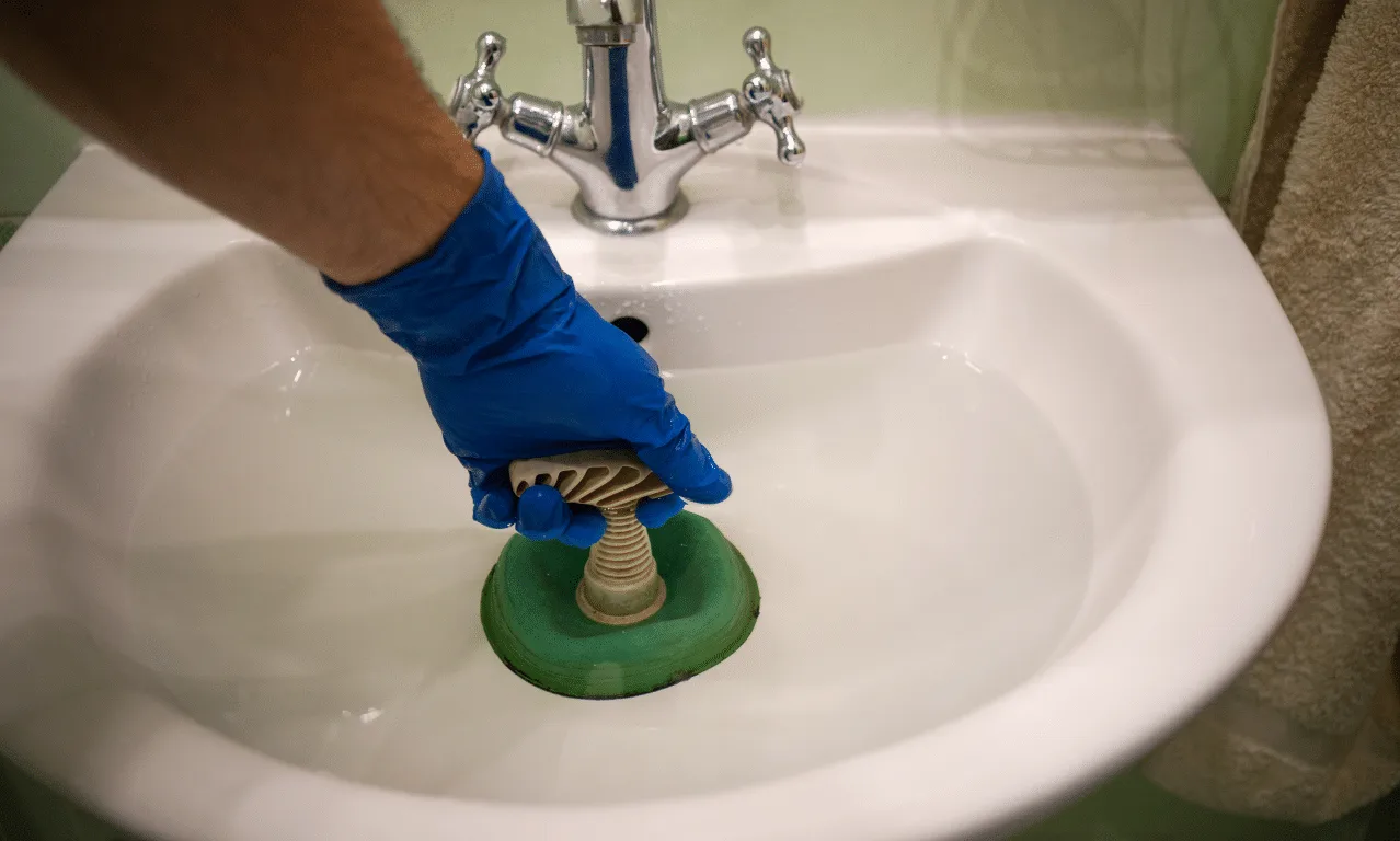 Gloved hand clearing a bathroom sink drain