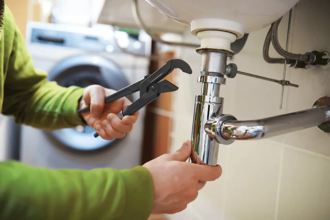 Plumber tightening a sink drain trap with a pipe wrench
